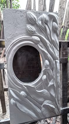 a white sculpture with flowers on it sitting in front of a wooden fence and trees