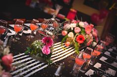 a table topped with lots of glasses filled with flowers and wineglasses next to each other