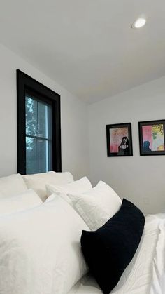 a bed with white sheets and pillows in a bedroom next to two pictures on the wall