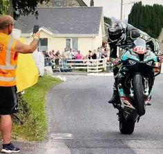 a man on a motorcycle taking a photo with his cell phone while people watch from the side of the road