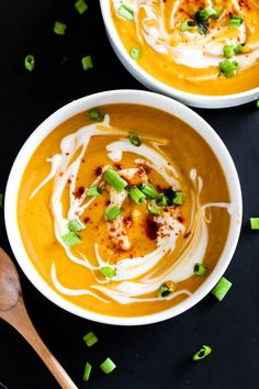 two white bowls filled with carrot soup and topped with sour cream, scallops and green onions