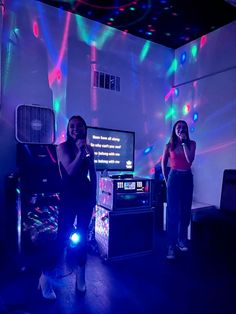 two women standing in front of a tv with colorful lights on the wall behind them