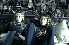 two young women sitting on the floor in front of a wall full of stuffed animals