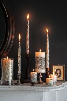 candles are lit in front of a mirror and framed pictures on a shelf with an ornate frame