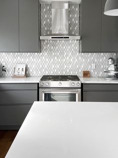 a kitchen with gray cabinets and white counter tops, stainless steel oven hood over the stove