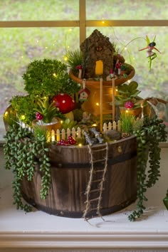 a wooden bucket filled with lots of plants and fairy figurines on top of a window sill