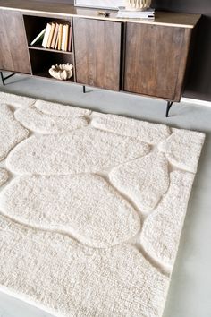 a white rug on top of a floor next to a wooden cabinet and book shelf