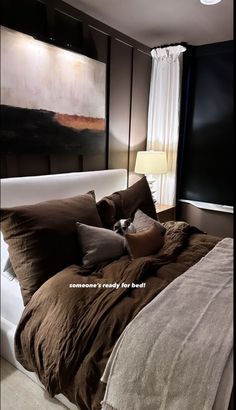 the bed is made with brown linens and pillows, along with a painting on the wall