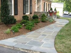 a brick house with plants and flowers in the front yard, along side a stone walkway