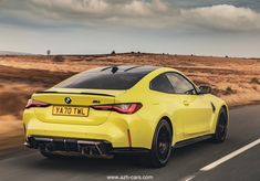 the rear end of a yellow bmw z4 roadster driving on a country road