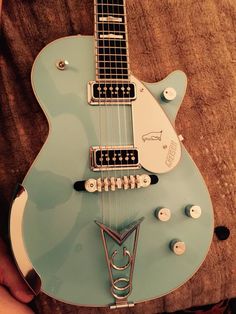 a blue electric guitar sitting on top of a wooden table next to a person's hand