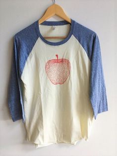 "Hand Printed and Hand Drawn! This is a raglan baseball tee printed with a hand drawn apple. The shirt shown here is naturat with triblend navy blue sleeves. // PROCESS: All of our items are individually hand printed by either me or my dad, which can lead to slight variations in placement. The ink is heat cured and will not fade over time. Since our items are printed to order, there is a 1-2 week processing time before shipping. If you absolutely need an item shipped quicker than that, please me Apple Shirt, Summer Shopping List, Food Shirt, Gardening Gift, Coffee Sweatshirt, Screen Printing Shirts, Raglan Shirt, Raglan Shirts, Blue Tshirt