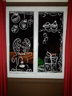 a window with christmas decorations drawn on the glass and red curtains in front of it