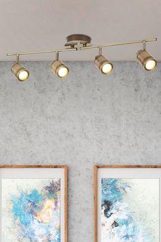 three lights are hanging above two paintings on the wall