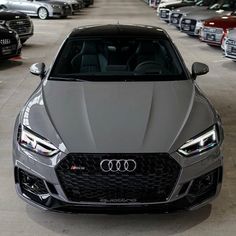 the front end of a grey car parked in a parking lot with other cars behind it