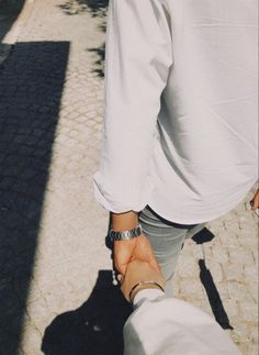 two people holding hands while walking down the street with their shadows on the ground behind them