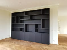 an empty room with black bookshelves in the middle and wood flooring on the other side