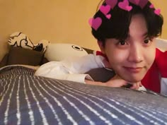 a young man laying on top of a bed wearing a pink heart headband and smiling at the camera