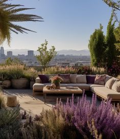 a couch sitting on top of a patio next to purple flowers and trees in front of a cityscape