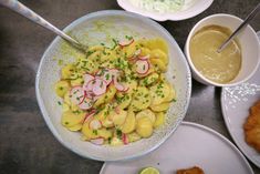 a bowl filled with food next to two bowls of sauce and other dishes on the table