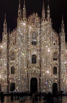 people are standing in front of a large building that has lights all over it and is lit up