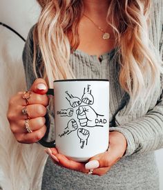 a woman holding a coffee mug with drawings on it