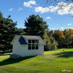 a small white shed sitting on top of a lush green field under a blue sky