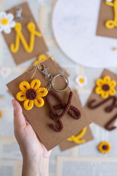 a person holding up a piece of paper with flowers on it and the letter w is made out of yarn