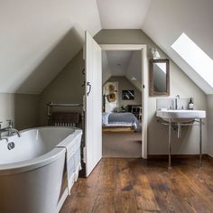 a bathroom with a tub, sink and mirror in the corner next to an attic bedroom