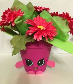 a pink flower pot sitting on top of a table next to green leaves and flowers