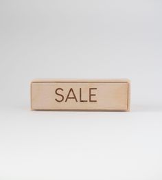 a wooden block with the word sale written in black ink on it, against a white background