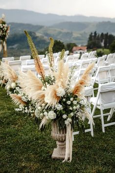 an arrangement of flowers and pamodia in a vase on the grass at a wedding ceremony