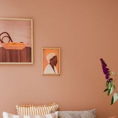 a bedroom with pink walls and pictures on the wall, including a bed in front of a flower vase