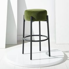 a green stool sitting on top of a white floor next to a tall wall and window