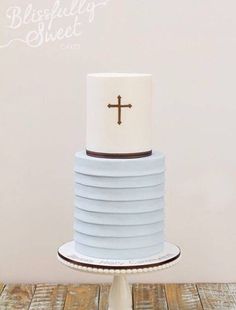 a blue and white cake with a cross on top is sitting on a stand in front of a wall