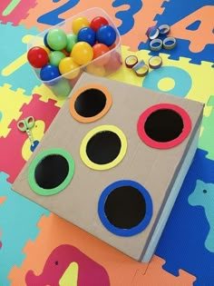 a cardboard box filled with lots of different colored balls next to some scissors and other toys