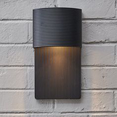 an outdoor wall light on the side of a white brick building with a black cylinder shade