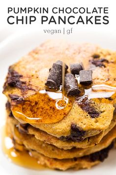 a stack of pancakes with chocolate chips and syrup being poured onto them on a white plate