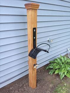 a wooden post with a black handle attached to it next to a flower bed and house