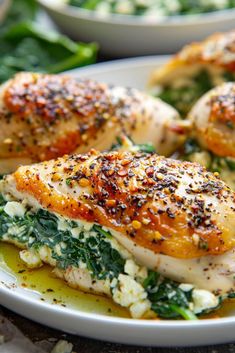 two white plates topped with chicken covered in cheese and spinach next to other dishes