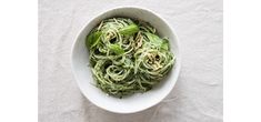 a white bowl filled with green pasta on top of a table