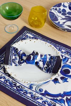 a blue and white plate with a bow tie on it next to other plates, cups and glasses