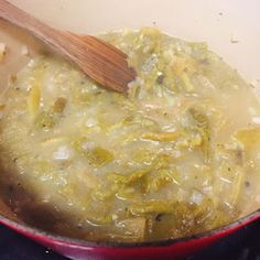 a wooden spoon in a red pot filled with green vegetables and sauce on top of a stove