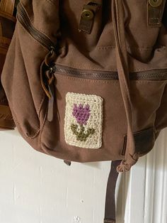 a brown purse with a crocheted flower on it hanging from a hook in front of a door