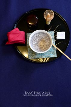 a black plate topped with a white bowl and chopsticks