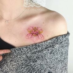 a woman's shoulder with a pink flower tattoo on the left side of her chest