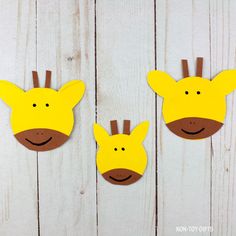 three paper giraffes are hanging on a white wooden wall, one is yellow and the other is brown