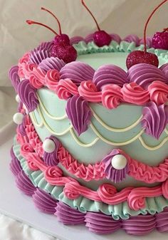 a cake decorated with pink, purple and green icing has cherries on top