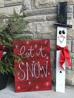 a snowman made out of wood next to a sign that says let it snow