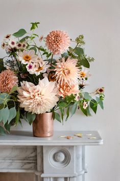 a vase filled with lots of flowers on top of a table next to a fireplace